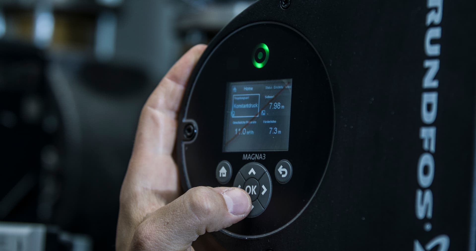 Hand stellt eine Grundfos-Umwälzpumpe über das Bedienfeld mit Display ein.
