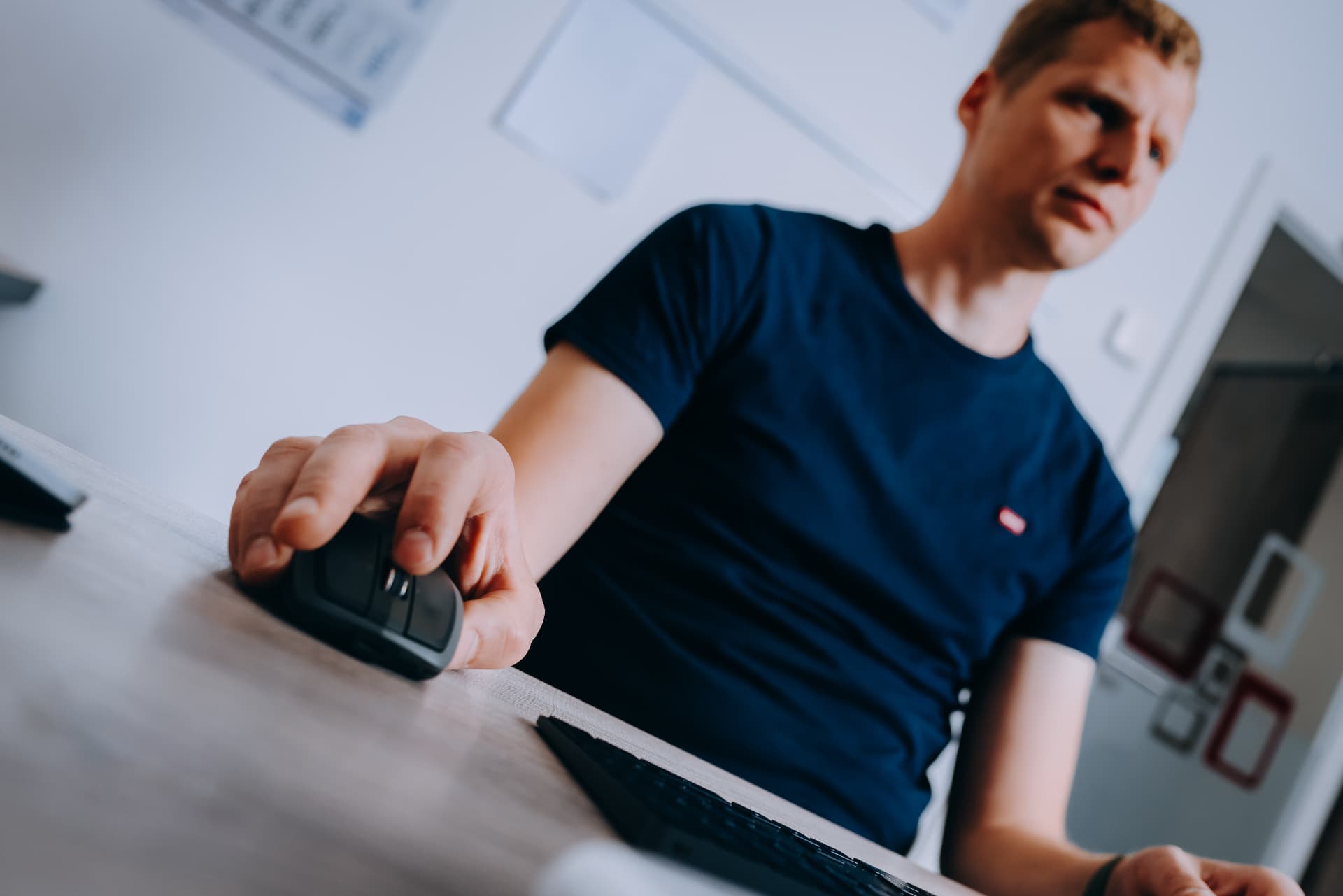 Wurm-Mitarbeiter bedient eine Computermaus am Büroschreibtisch; seine Hand und die Maus sind im Vordergrund zu sehen.