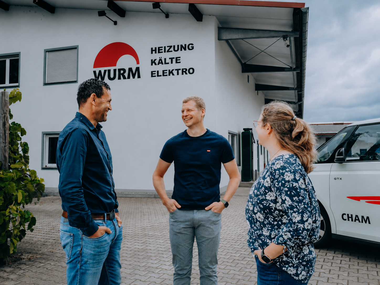 Die drei Mitglieder der Wurm-Geschäftsführung stehen im Gespräch vor dem Firmengebäude; daneben parkt ein Firmenfahrzeug.