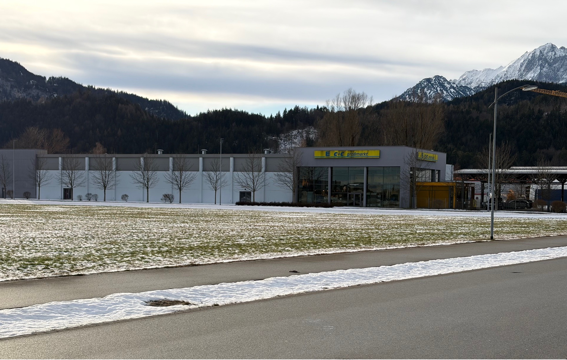 Außenansicht des Neubaus des C+C Großmarkts in Füssen mit Hallenfassade und verglastem Eingangsbereich vor Alpenkulisse.