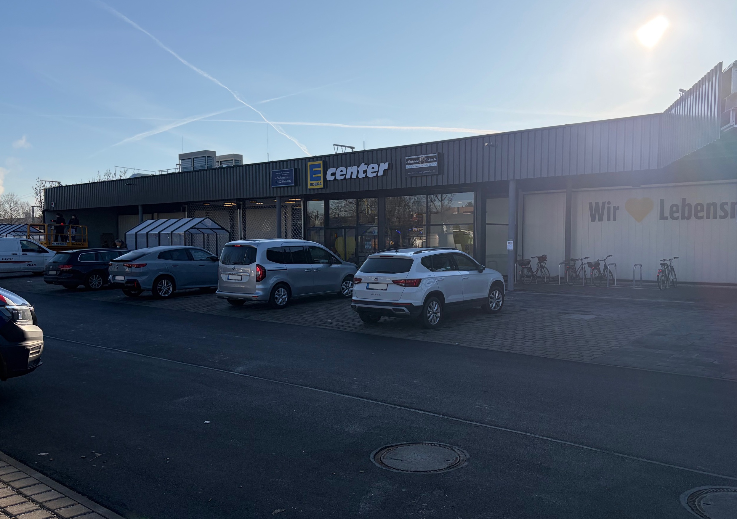 Außenansicht des Lebensmittelmarkts Edeka München mit Kundenparkplatz und Eingangsbereich.