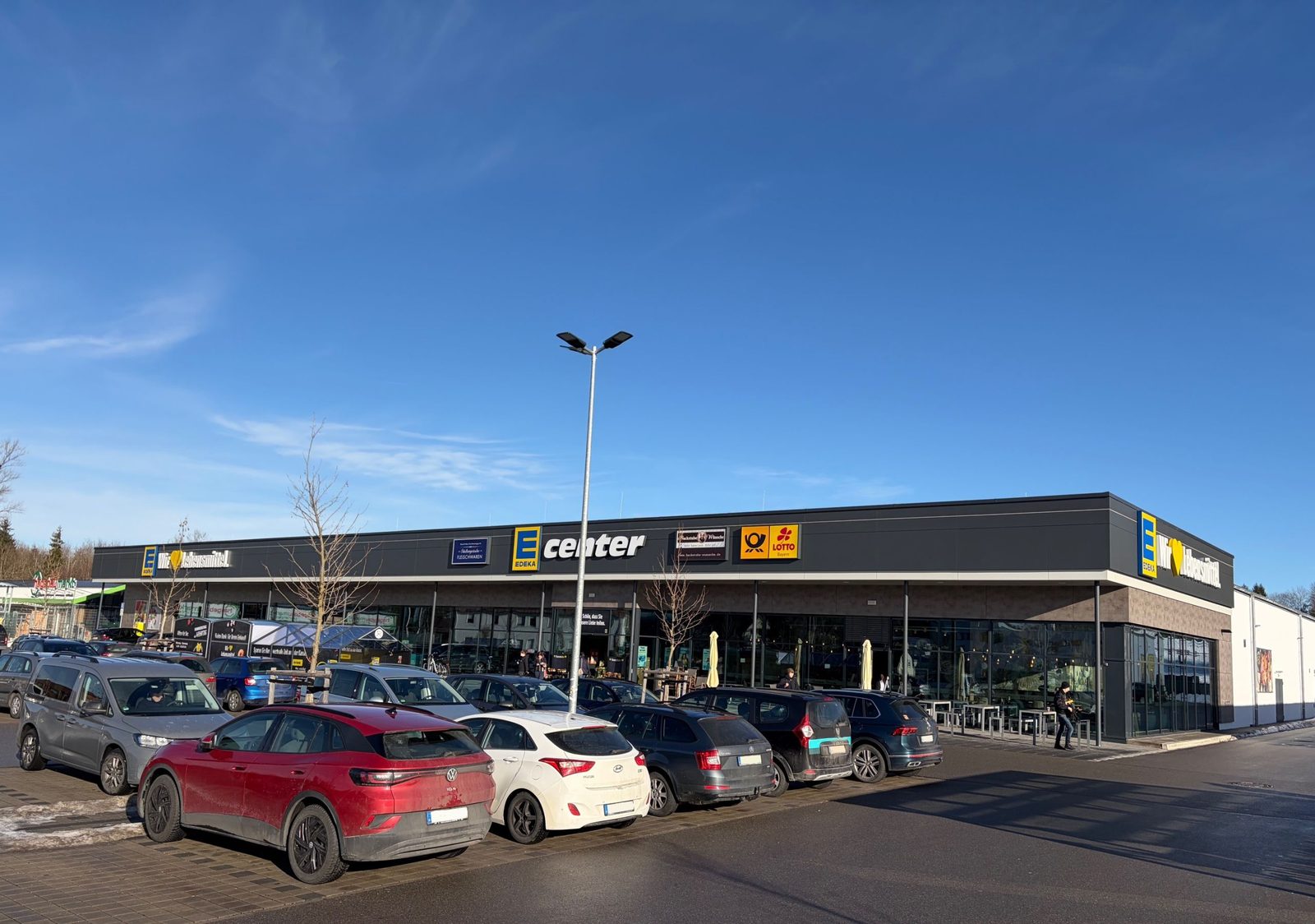 Außenansicht des neu errichteten Lebensmittelmarkts Edeka Penzberg in Penzberg mit vorgelagertem Parkplatz.