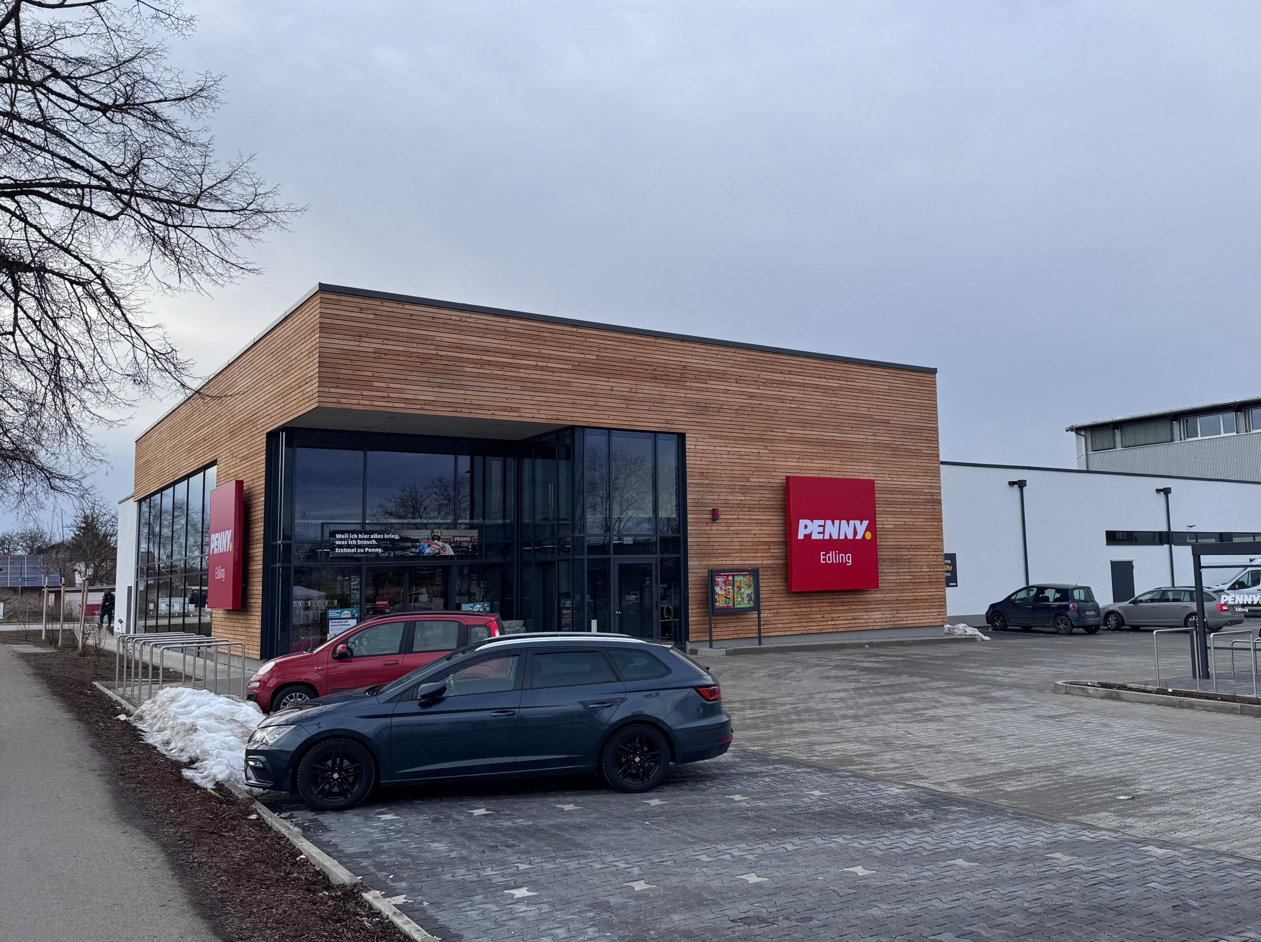 Neubau des Penny-Marktes in Edling mit Holzfassade, Glasfront und Parkplatz.