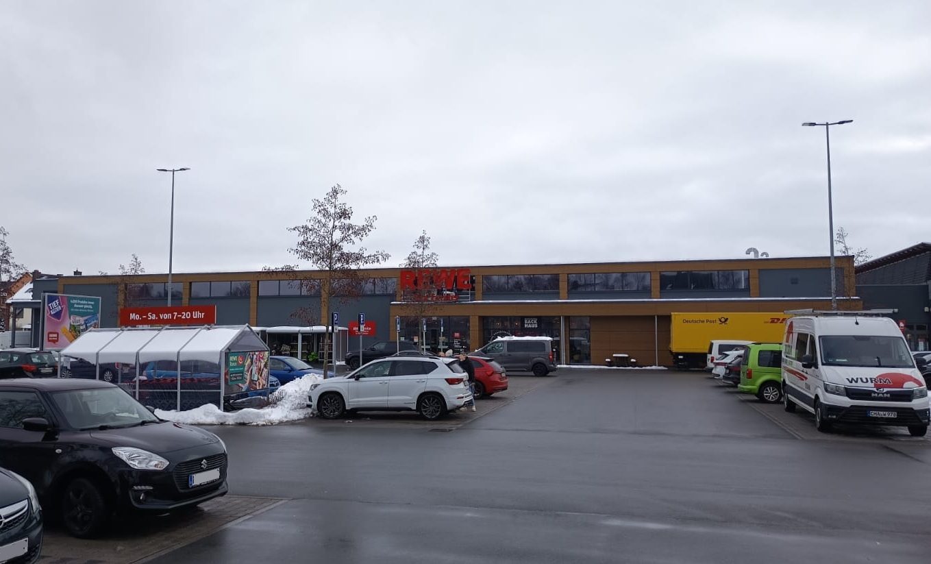 Außenansicht des neu errichteten Markts Rewe Münchberg mit Kundenparkplatz und Servicefahrzeug.