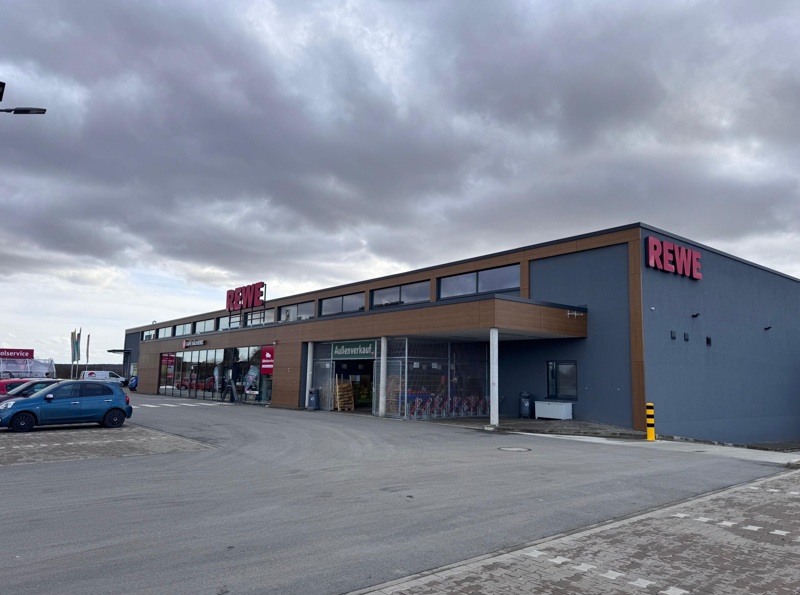 Außenansicht des neu errichteten Rewe-Marktes in Sünching mit Parkplatz und Eingangsbereich.